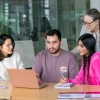 a group of 3 college students and a professor huddled around a laptop