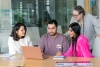 a group of 3 college students and a professor huddled around a laptop