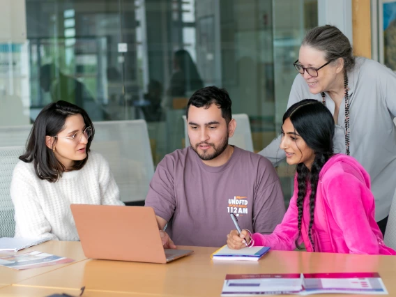 a group of 3 college students and a professor huddled around a laptop