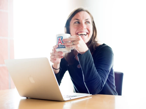 University of Arizona student smiling with laptop and coffee mug. 