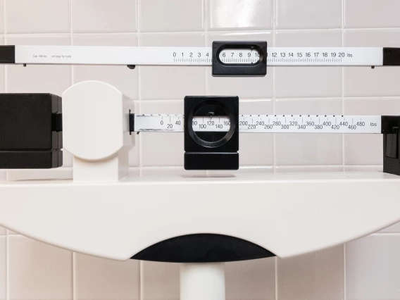 Close-up of a white mechanical balance scale in front of a white tile background