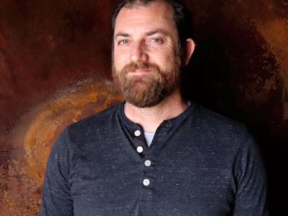 SNSW Head Brewer Patrick Heacock poses in front of a brown backdrop.