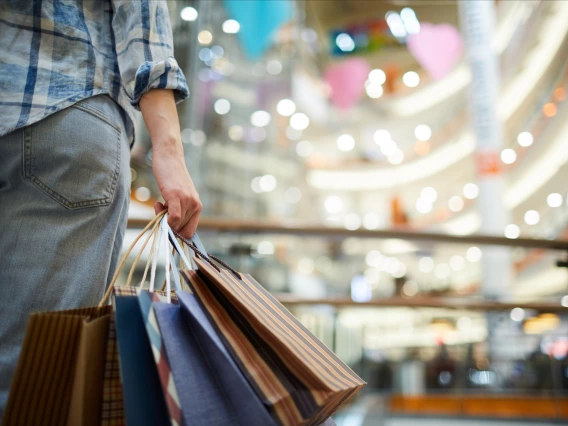 A woman stands in a mall holding shopping bags
