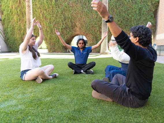 A CALES Student Wellness Ambassador leads a group in yoga on the grass within CALES courtyard.