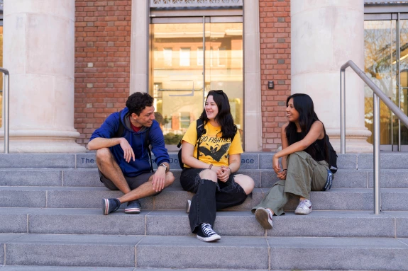 A group of students laughing and talking on the steps of the Forbes Building.