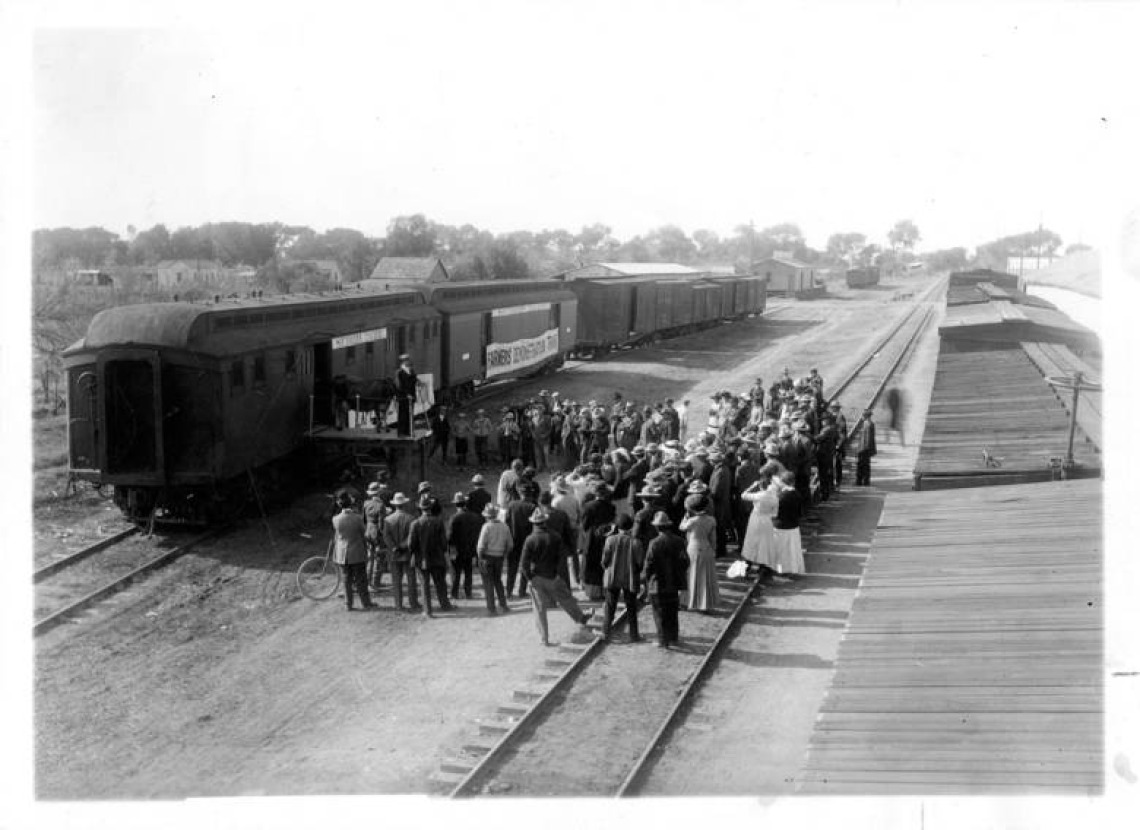 Agriculture Experiment Station Demonstration Train at Mesa, Arizona. Man is standing on a train platform with a cow talking to a group of farmers.