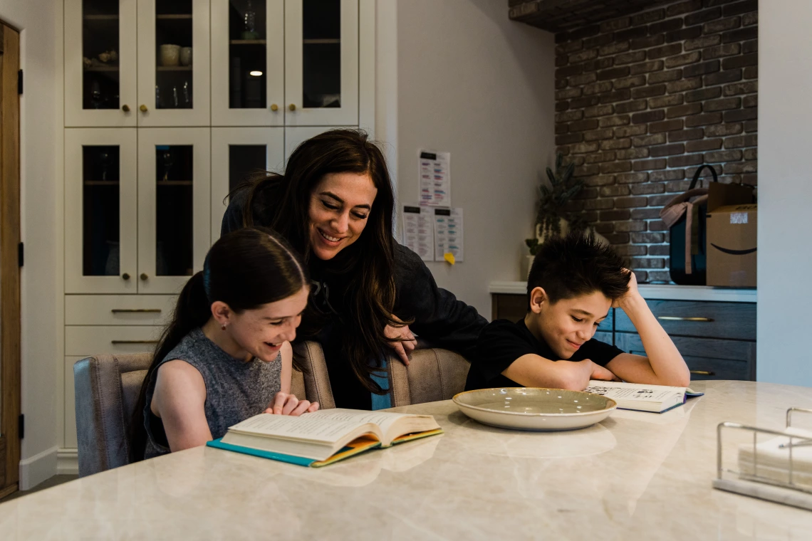 A mother helps her children do homework at a kitchen counter