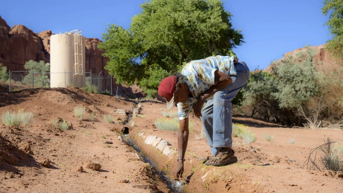 a man leaning over a small stream of water on the Navajo Nation