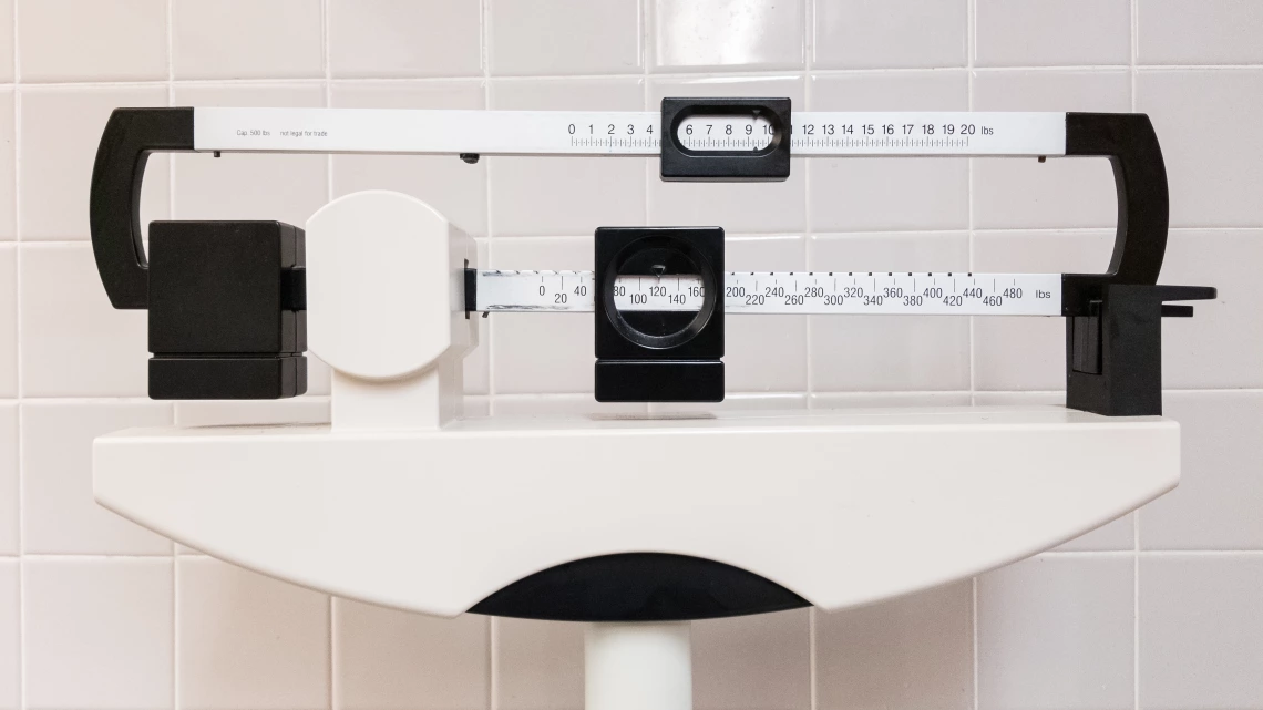 Close-up of a white mechanical balance scale in front of a white tile background