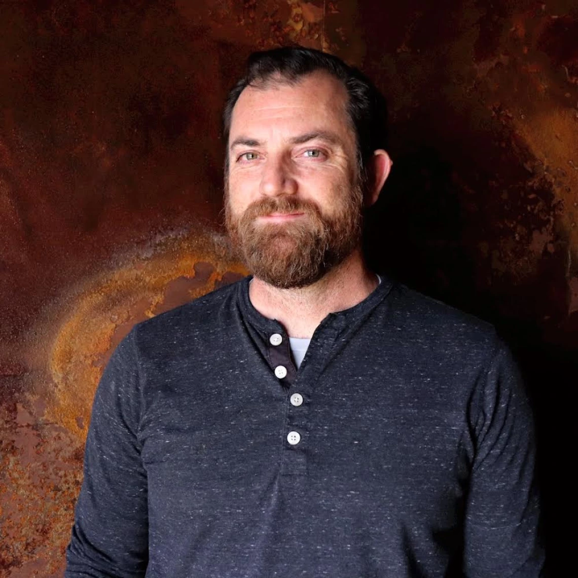 SNSW Head Brewer Patrick Heacock poses in front of a brown backdrop.