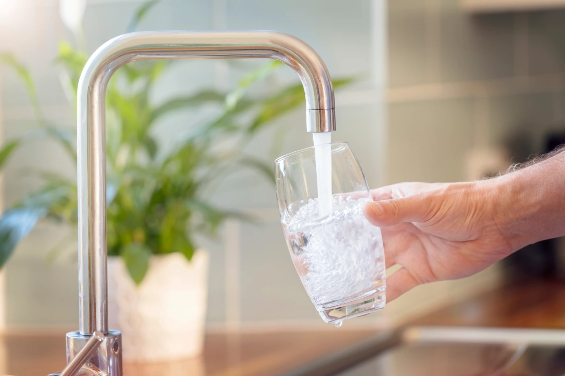 A person fills a drinking glass from the kitchen tap