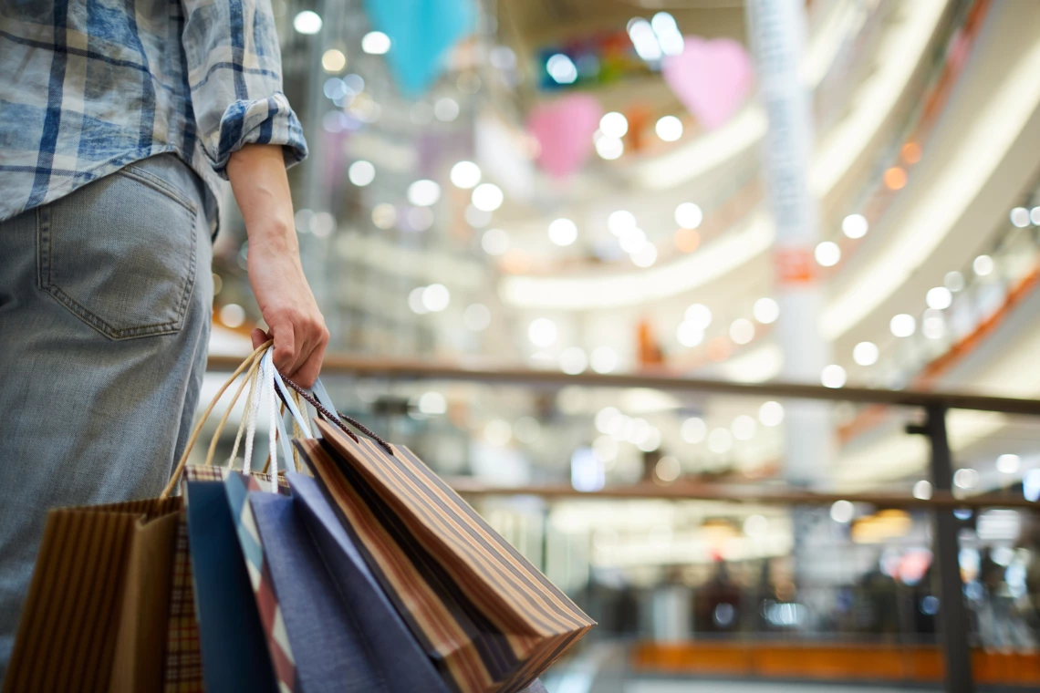A woman stands in a mall holding shopping bags
