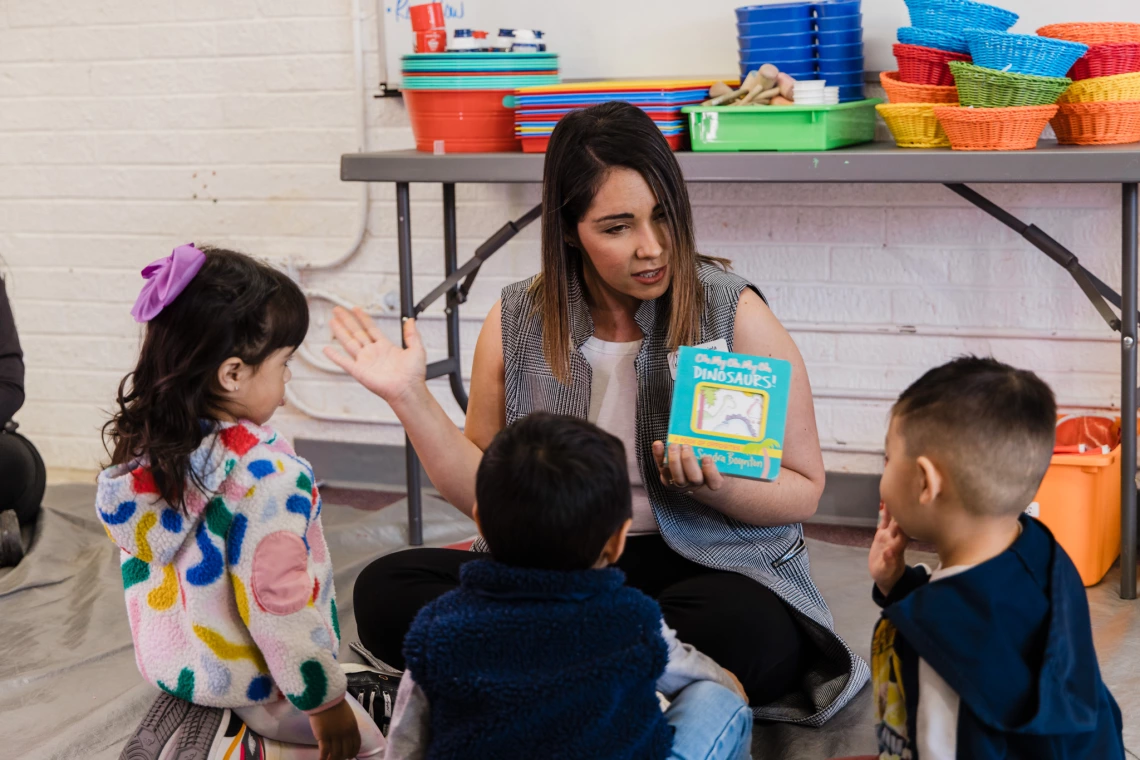 A teacher reads a board book to a group of young children