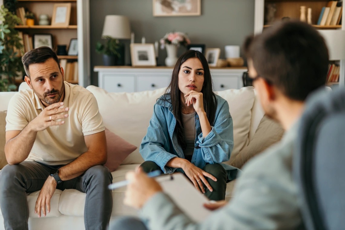 A heterosexual couple sits on a couch across from their therapist