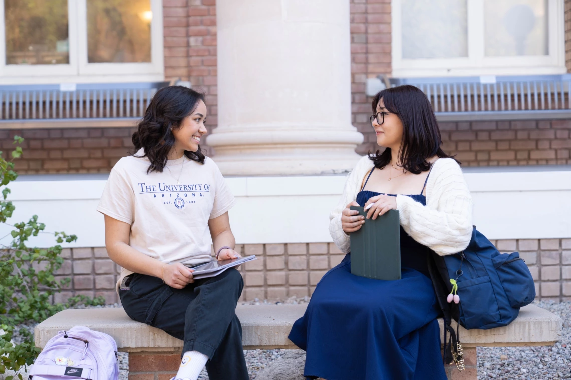 two women sittting on a bench outside having a conversation