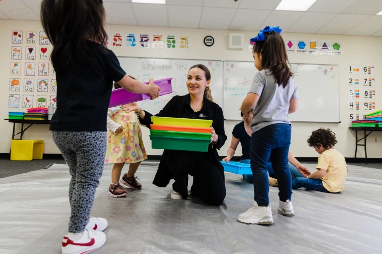 A teacher collects bins from her class of young children