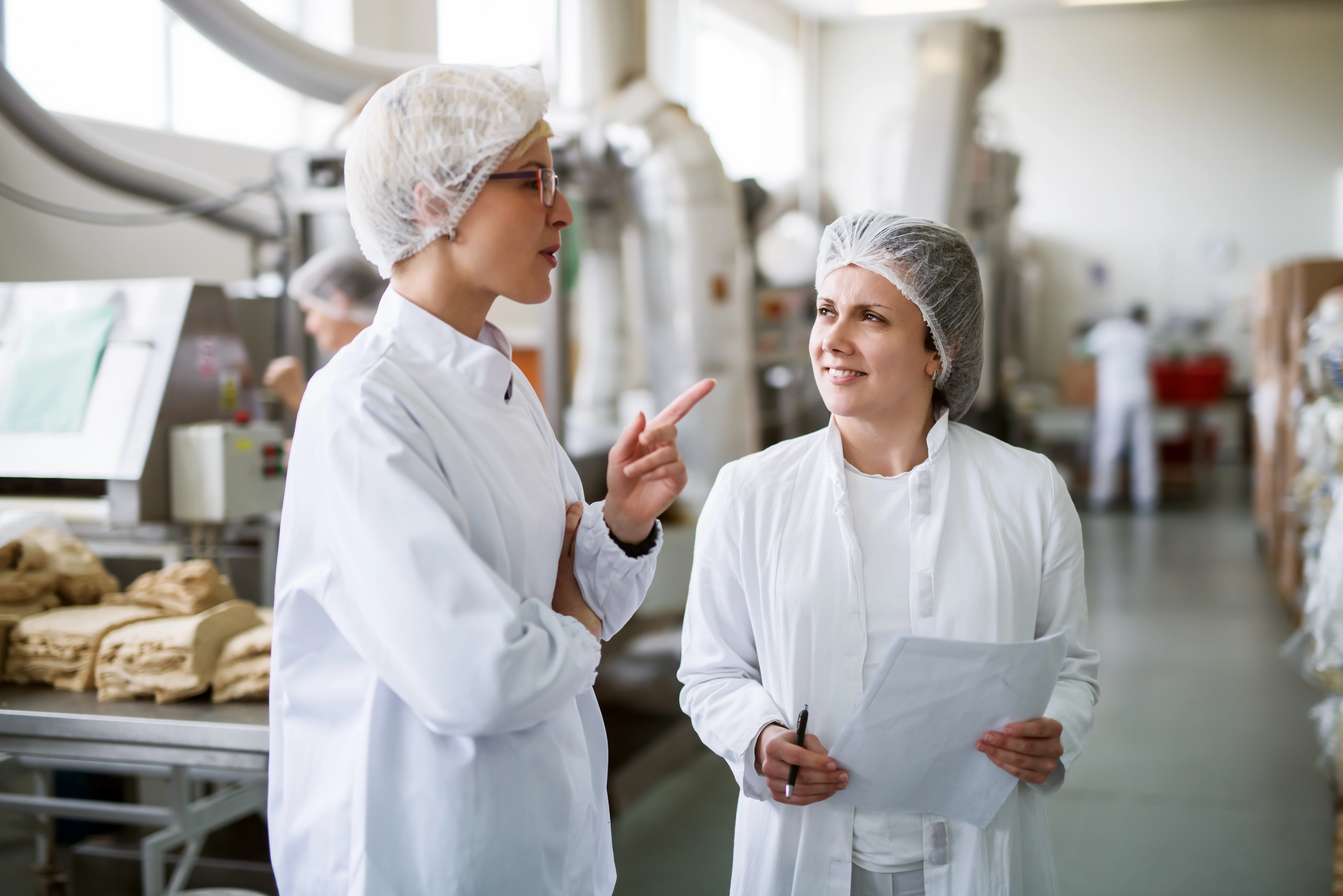 Two people wearing lab coats and hair protectors in a food processing lab.