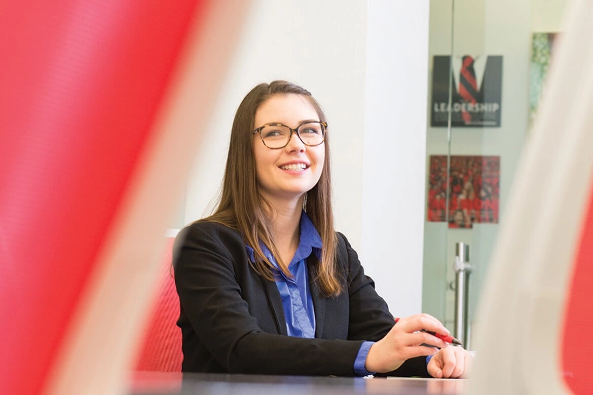 Student in professional attire sitting in a boardroom.