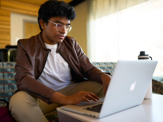 Young male college student sitting on a couch with his laptop