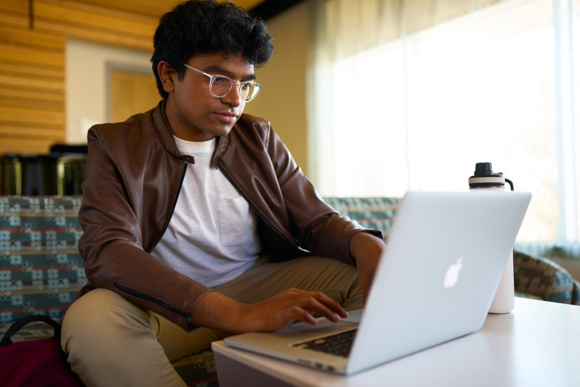 Young male college student sitting on a couch with his laptop